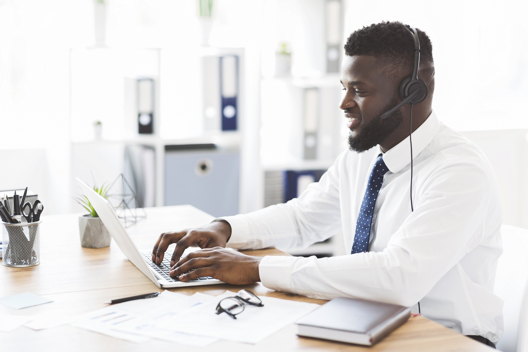 Happy african american office worker helping clients, using laptop, copy space